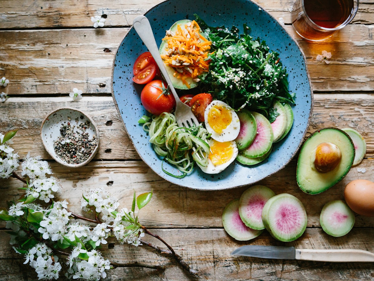Plato saludable con verduras frescas, huevo y aguacate sobre una mesa de madera.